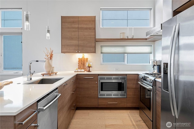 kitchen with brown cabinets, a peninsula, appliances with stainless steel finishes, and a sink
