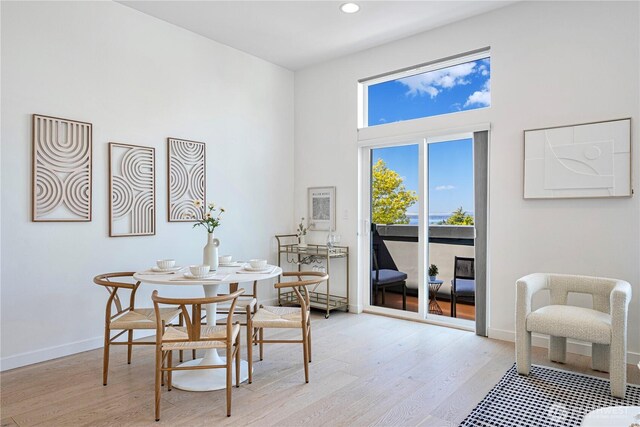 dining room featuring baseboards, recessed lighting, light wood-style flooring, and a towering ceiling