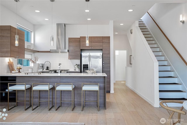 kitchen with a breakfast bar area, modern cabinets, light wood-type flooring, stainless steel fridge, and wall chimney exhaust hood