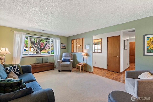 carpeted living area with baseboards, a textured ceiling, and visible vents