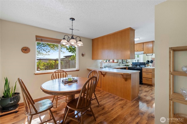 kitchen with a textured ceiling, black electric range oven, wood finished floors, light countertops, and a peninsula