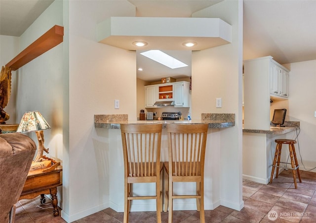 kitchen with white cabinets, a breakfast bar area, baseboards, under cabinet range hood, and a skylight