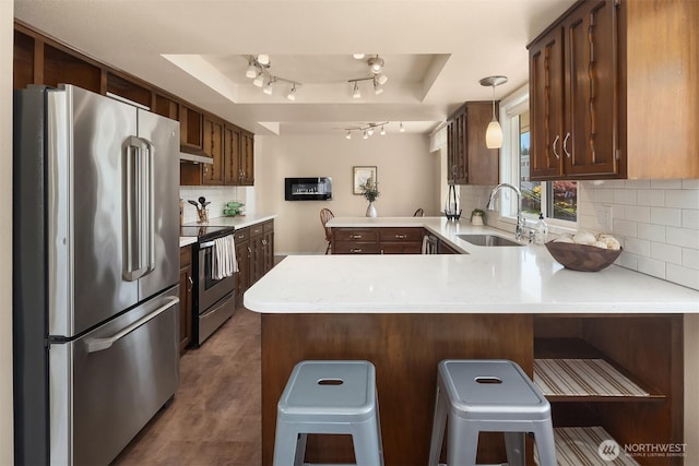 kitchen with a peninsula, light countertops, under cabinet range hood, a sink, and stainless steel appliances