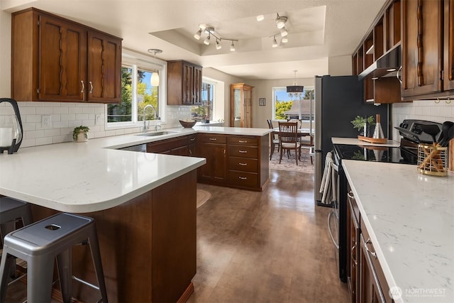 kitchen featuring a sink, stainless steel range with electric stovetop, light countertops, a peninsula, and a tray ceiling