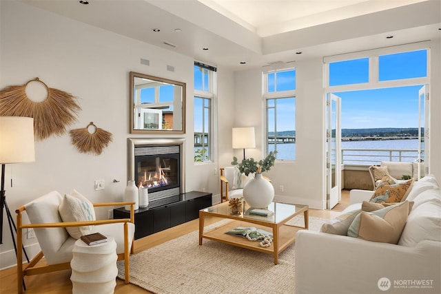 living room featuring recessed lighting, a glass covered fireplace, a water view, and light wood-style floors