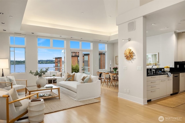 living area featuring light wood-type flooring, baseboards, a raised ceiling, a water view, and recessed lighting