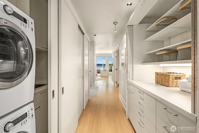 laundry room with stacked washer and clothes dryer, light wood-style flooring, recessed lighting, and cabinet space