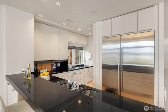 kitchen featuring visible vents, recessed lighting, stainless steel built in fridge, white cabinets, and dark stone countertops