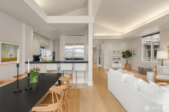 living area featuring light wood-type flooring, recessed lighting, a raised ceiling, and baseboards