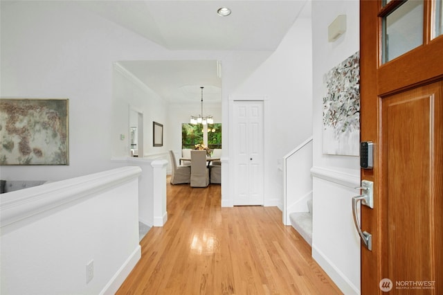 hallway with baseboards, an inviting chandelier, and light wood finished floors