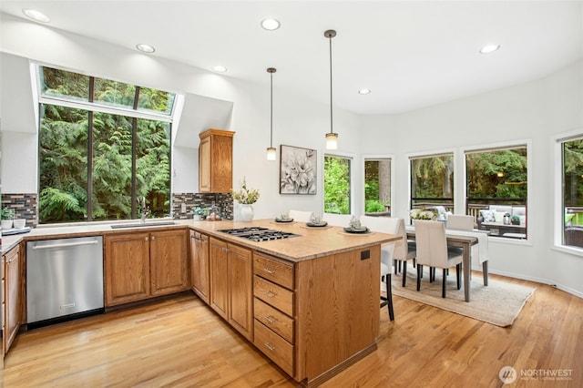kitchen with tasteful backsplash, a sink, light countertops, light wood-style floors, and stainless steel appliances