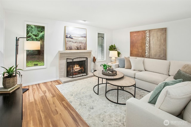 living room featuring baseboards, a brick fireplace, and wood finished floors