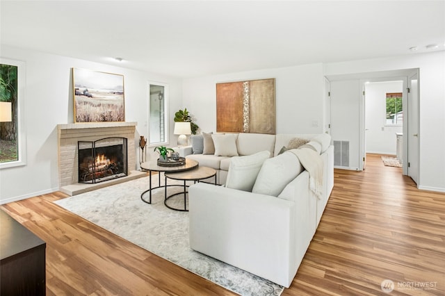 living area with a fireplace, baseboards, visible vents, and light wood-type flooring