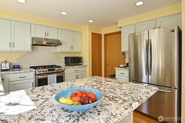 kitchen with backsplash, light stone countertops, under cabinet range hood, stainless steel appliances, and recessed lighting