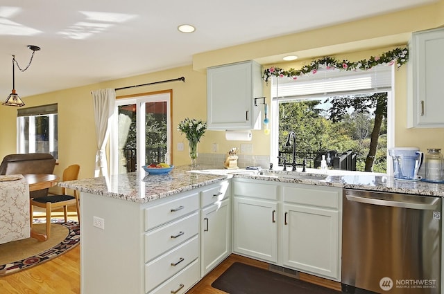 kitchen with light stone countertops, a sink, a peninsula, wood finished floors, and stainless steel dishwasher