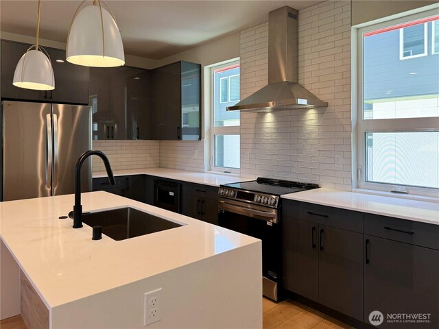 kitchen with decorative backsplash, a sink, light countertops, stainless steel appliances, and wall chimney exhaust hood