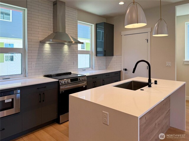 kitchen with wall chimney range hood, backsplash, stainless steel electric range oven, a sink, and light wood-style floors