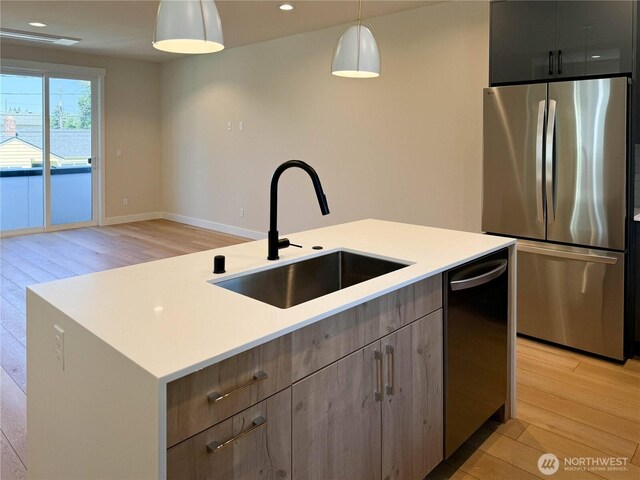 kitchen featuring pendant lighting, light wood-style floors, light countertops, a sink, and appliances with stainless steel finishes