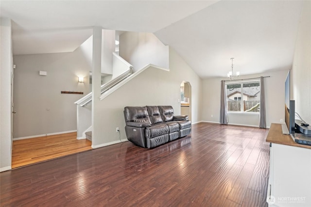 living area with arched walkways, vaulted ceiling, wood finished floors, a chandelier, and stairs