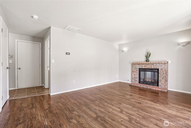 unfurnished living room with baseboards, visible vents, wood finished floors, and a fireplace