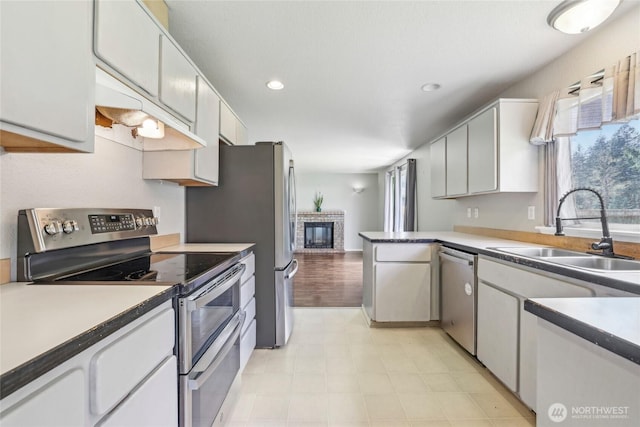 kitchen featuring a sink, appliances with stainless steel finishes, white cabinets, and a brick fireplace