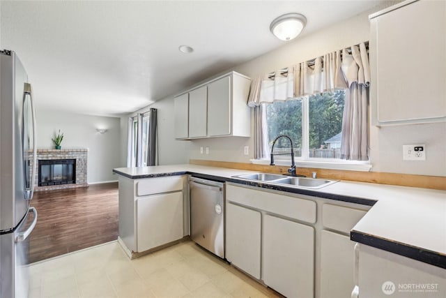 kitchen with a brick fireplace, a peninsula, open floor plan, a sink, and appliances with stainless steel finishes