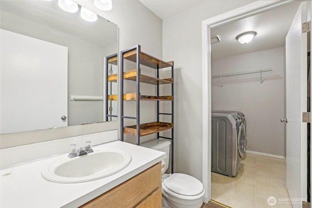 bathroom with washing machine and clothes dryer, a walk in closet, vanity, toilet, and tile patterned floors