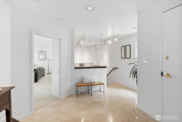 corridor featuring baseboards, light tile patterned floors, and an upstairs landing