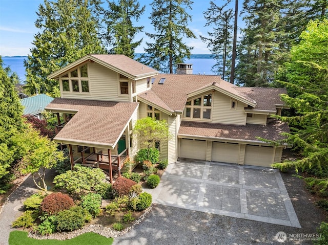 view of front facade with a chimney, a garage, concrete driveway, a water view, and a shingled roof