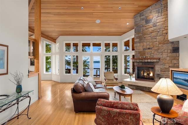 living room featuring baseboards, a stone fireplace, wooden ceiling, and wood finished floors
