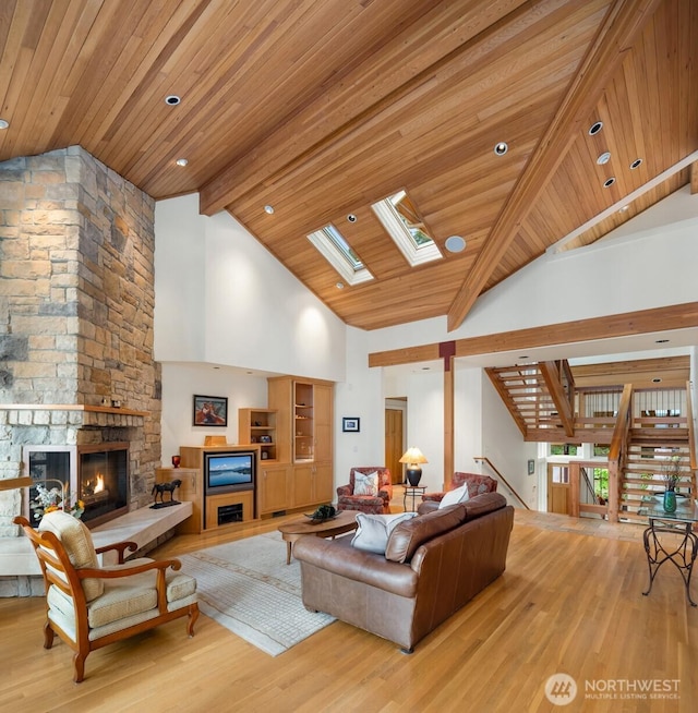 living area featuring beam ceiling, a fireplace, light wood-style floors, high vaulted ceiling, and a skylight