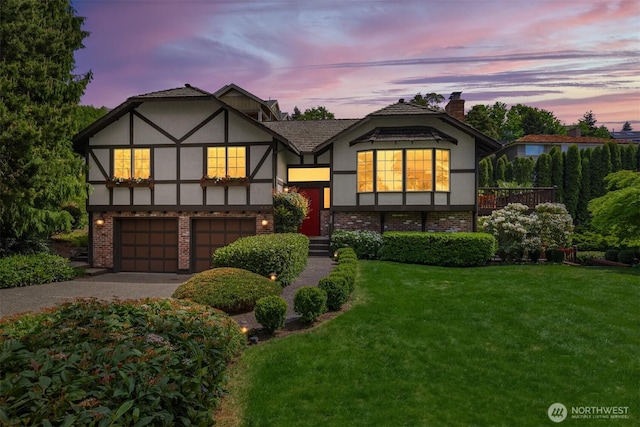 tudor house featuring a yard, an attached garage, driveway, and stucco siding