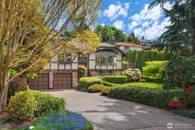 tudor house featuring brick siding, a garage, driveway, and stucco siding