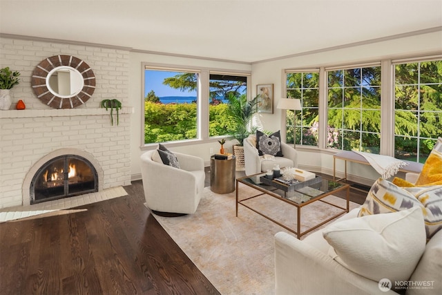 living area with crown molding, a brick fireplace, and wood finished floors