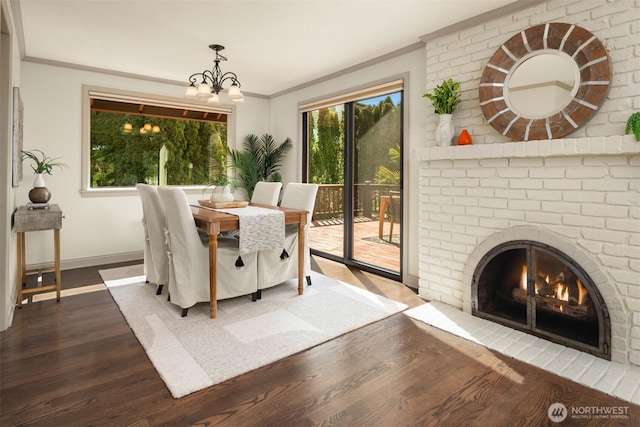 dining space featuring crown molding, a notable chandelier, a brick fireplace, baseboards, and dark wood-style floors