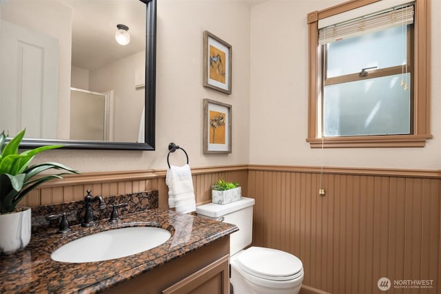 full bath featuring vanity, a stall shower, toilet, and a wainscoted wall