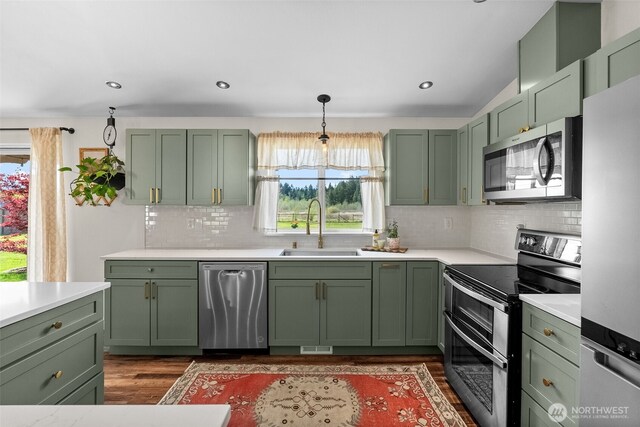kitchen featuring appliances with stainless steel finishes, wood finished floors, a sink, light countertops, and green cabinetry