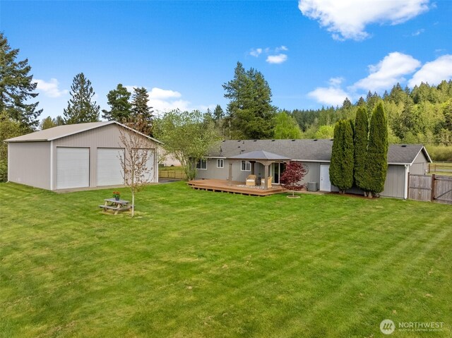 rear view of property featuring a lawn, a wooden deck, a garage, fence, and an outdoor structure