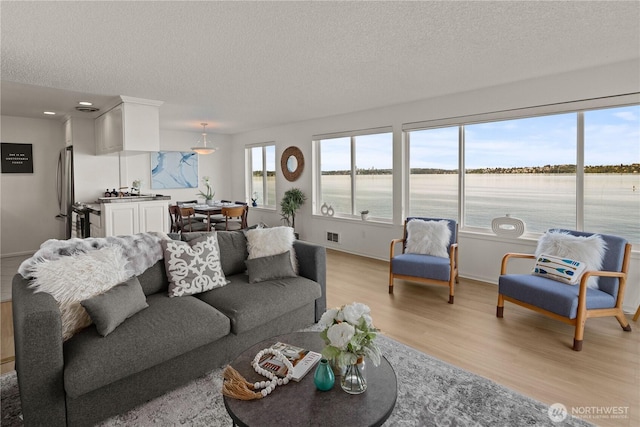 living area featuring a textured ceiling, light wood-style floors, a water view, and baseboards