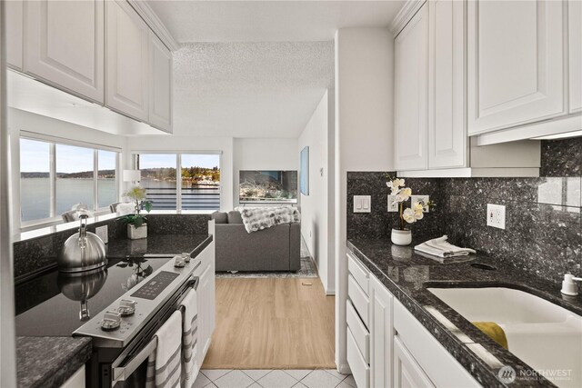 kitchen featuring stainless steel electric stove, a sink, white cabinets, a water view, and light tile patterned floors