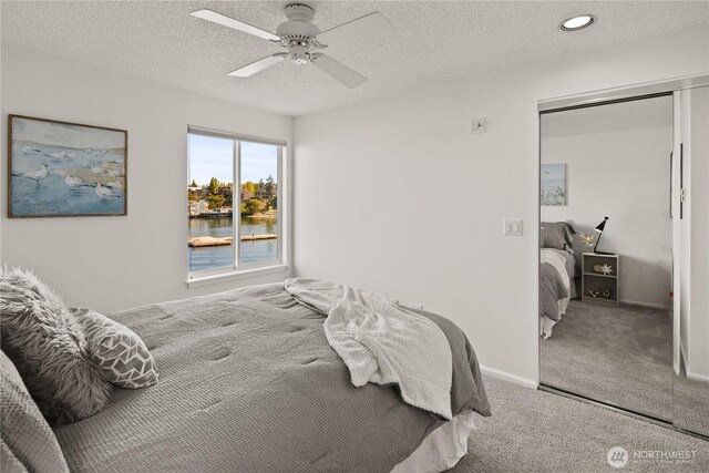 bedroom with carpet, a water view, a ceiling fan, a textured ceiling, and baseboards