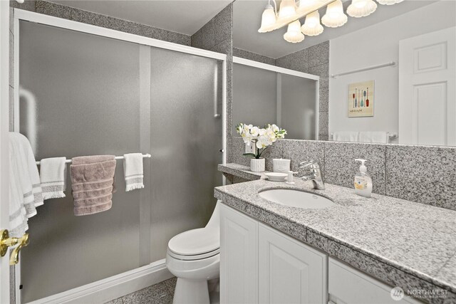 bathroom with toilet, vanity, a stall shower, and backsplash