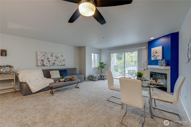 living area featuring a tiled fireplace, ceiling fan, and carpet flooring