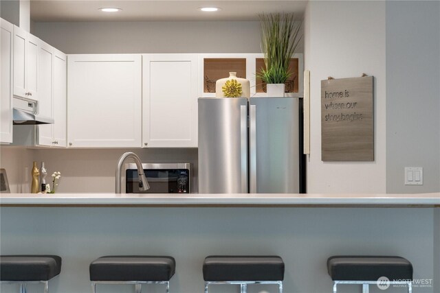 kitchen featuring a kitchen breakfast bar, appliances with stainless steel finishes, under cabinet range hood, recessed lighting, and white cabinetry