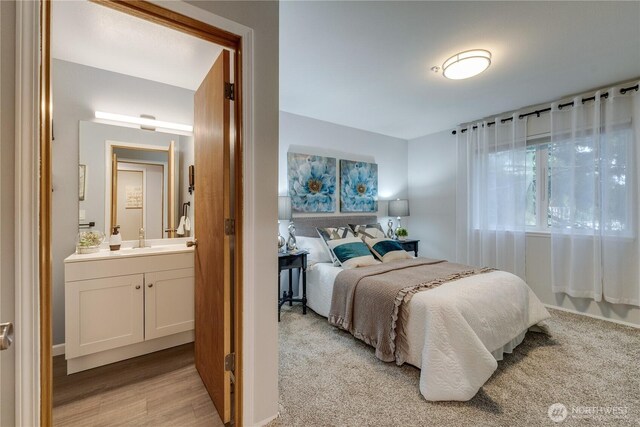 bedroom with connected bathroom, a sink, and light wood finished floors