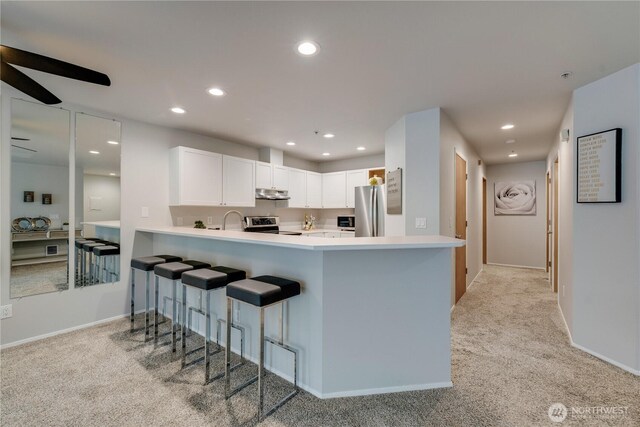 kitchen featuring light carpet, recessed lighting, light countertops, under cabinet range hood, and stainless steel appliances