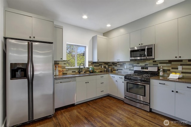 kitchen featuring a sink, backsplash, stainless steel appliances, and dark wood-style flooring