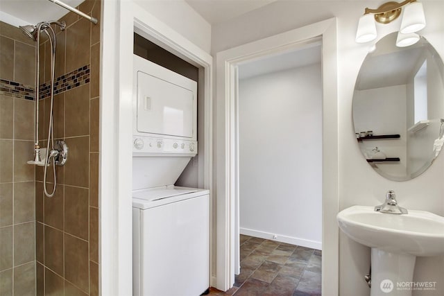 full bath featuring stacked washer and clothes dryer, baseboards, tiled shower, a sink, and stone finish flooring