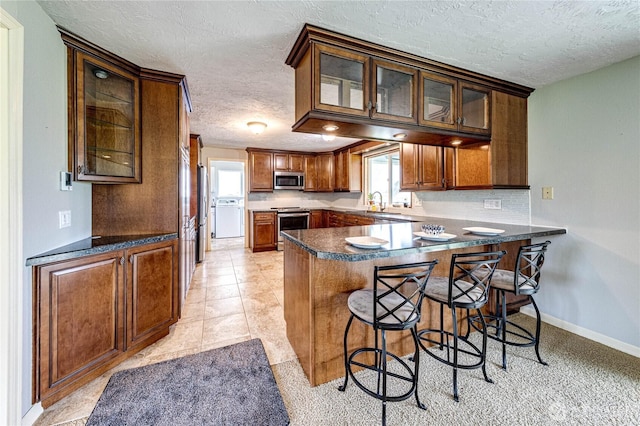 kitchen with a peninsula, glass insert cabinets, a breakfast bar area, a textured ceiling, and stainless steel appliances