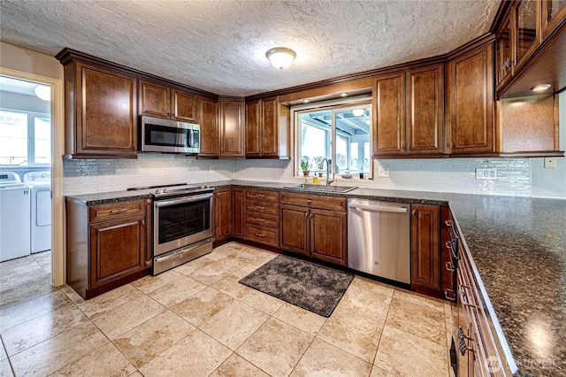kitchen featuring washer and dryer, appliances with stainless steel finishes, a healthy amount of sunlight, and a sink